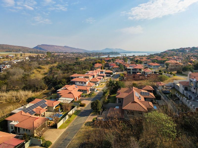 An aerial view of a residential estate featuring multiple homes with tiled roofs, solar panels, and surrounding natural landscape.
