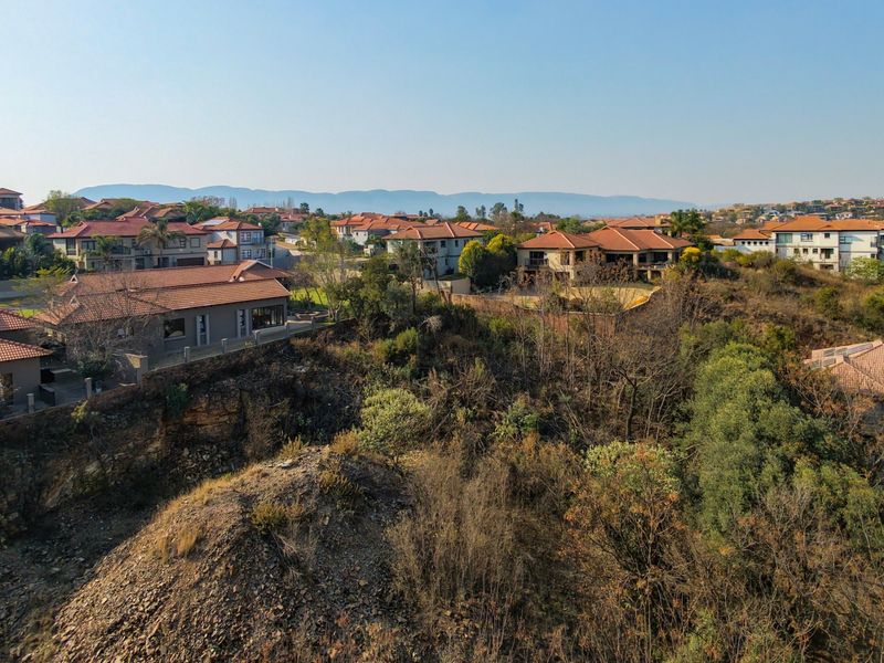 Aerial view of a residential estate featuring surrounding homes, natural vegetation, and rocky terrain.