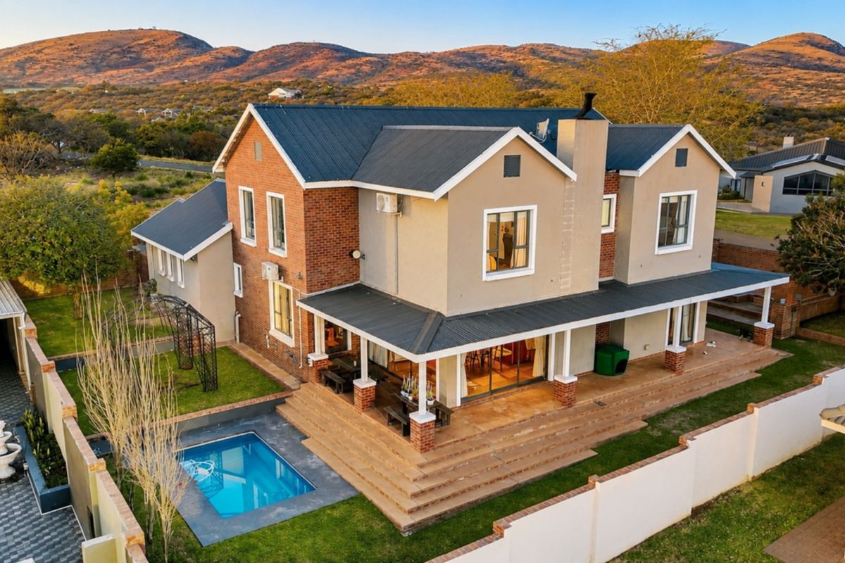 Aerial view of a double-story residence featuring a covered patio, swimming pool, and landscaped garden set against a scenic mountain backdrop.