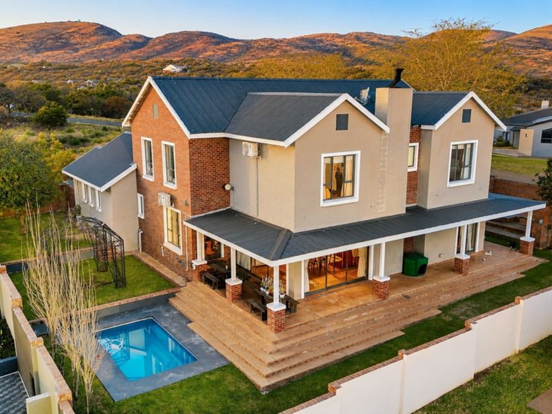 Aerial view of a double-story residence featuring a covered patio, swimming pool, and landscaped garden set against a scenic mountain backdrop.
