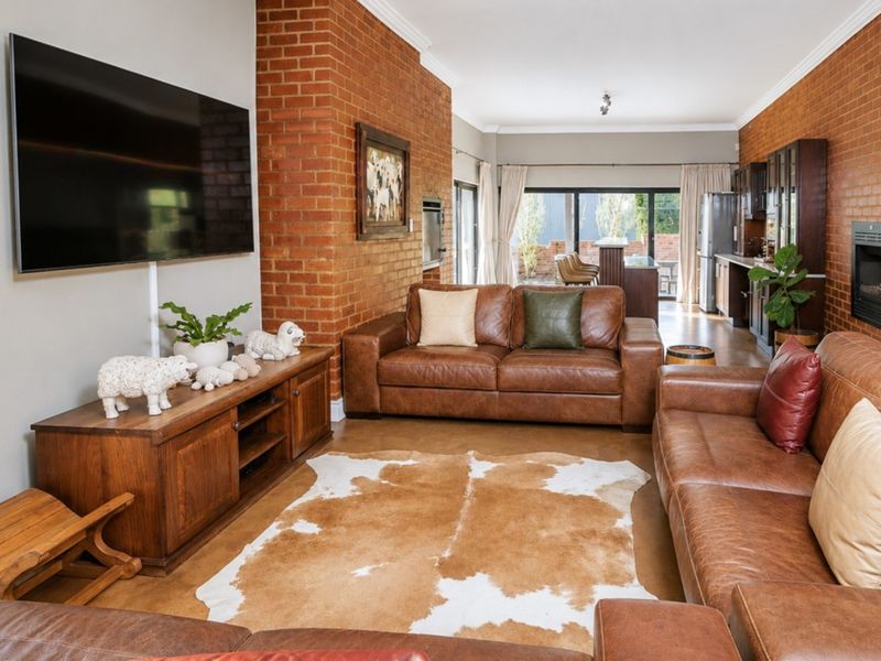 Spacious open-plan living area featuring exposed brick walls, a built-in fireplace, and seamless flow to the outdoor patio through large sliding glass doors.