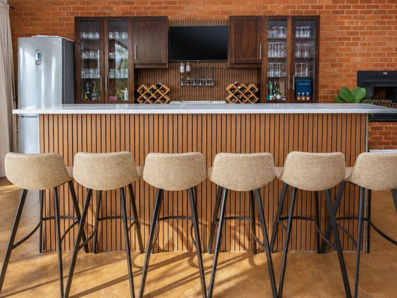 A well-appointed home bar featuring a timber-clad counter with stone top, built-in cabinetry, exposed brick wall, and a cozy integrated fireplace.