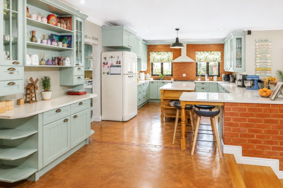Spacious kitchen featuring light green cabinetry, stone countertops, a central island, and an exposed brick feature wall with modern recessed lighting.