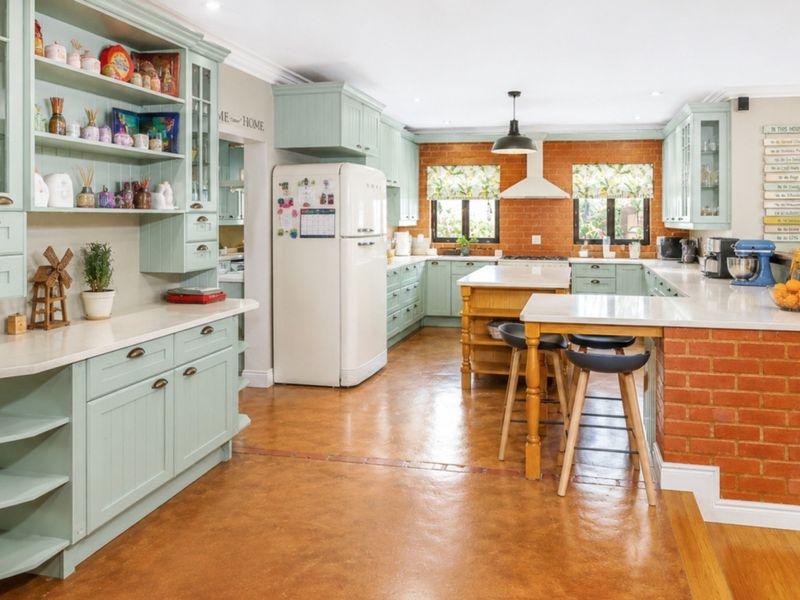 Spacious kitchen featuring light green cabinetry, stone countertops, a central island, and an exposed brick feature wall with modern recessed lighting.
