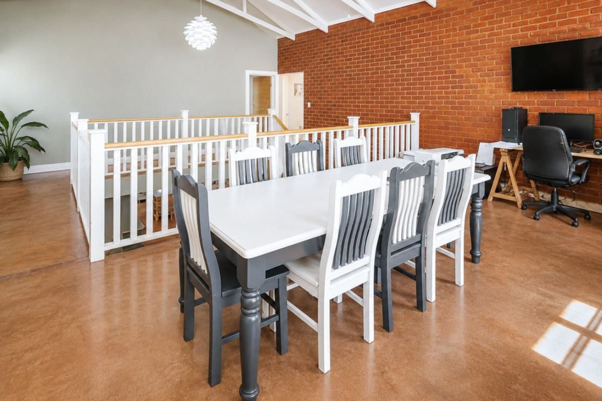 Spacious open-plan living area featuring a striking exposed brick wall, vaulted ceilings, and polished concrete flooring with a mezzanine-style timber balustrade.