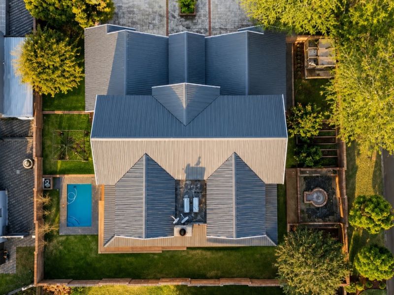 Aerial view of the property showcasing the metal roof structure, swimming pool, landscaped garden, and paved driveway areas.