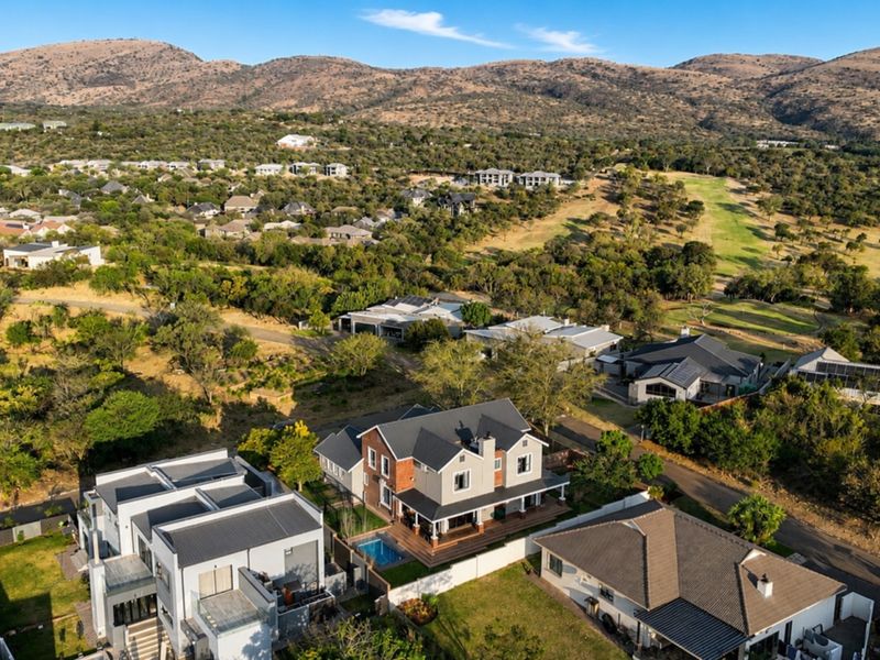 Aerial view of a residential property featuring a swimming pool, deck, and solar panels, situated within a scenic estate landscape.