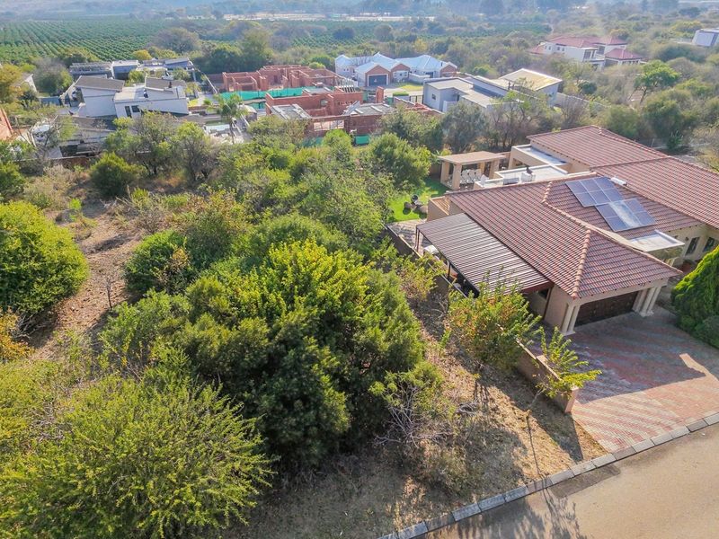 Aerial view of a residential property featuring a tiled roof with solar panels, a paved driveway, and established garden surroundings in a suburban estate.