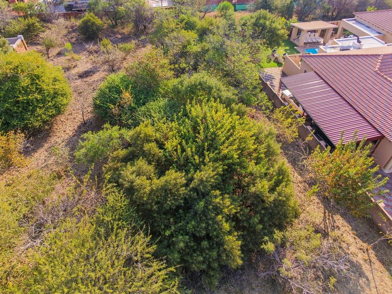 Aerial view of a residential property featuring a large garden, paved driveway, tiled roof with solar panels, and a swimming pool with a covered patio.