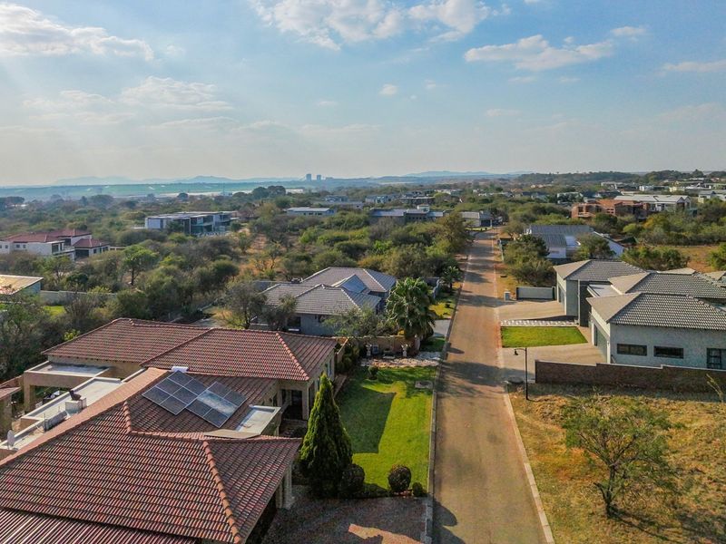 Aerial view of a residential estate featuring well-maintained homes with tiled roofs, solar panels, and landscaped gardens along a paved street.