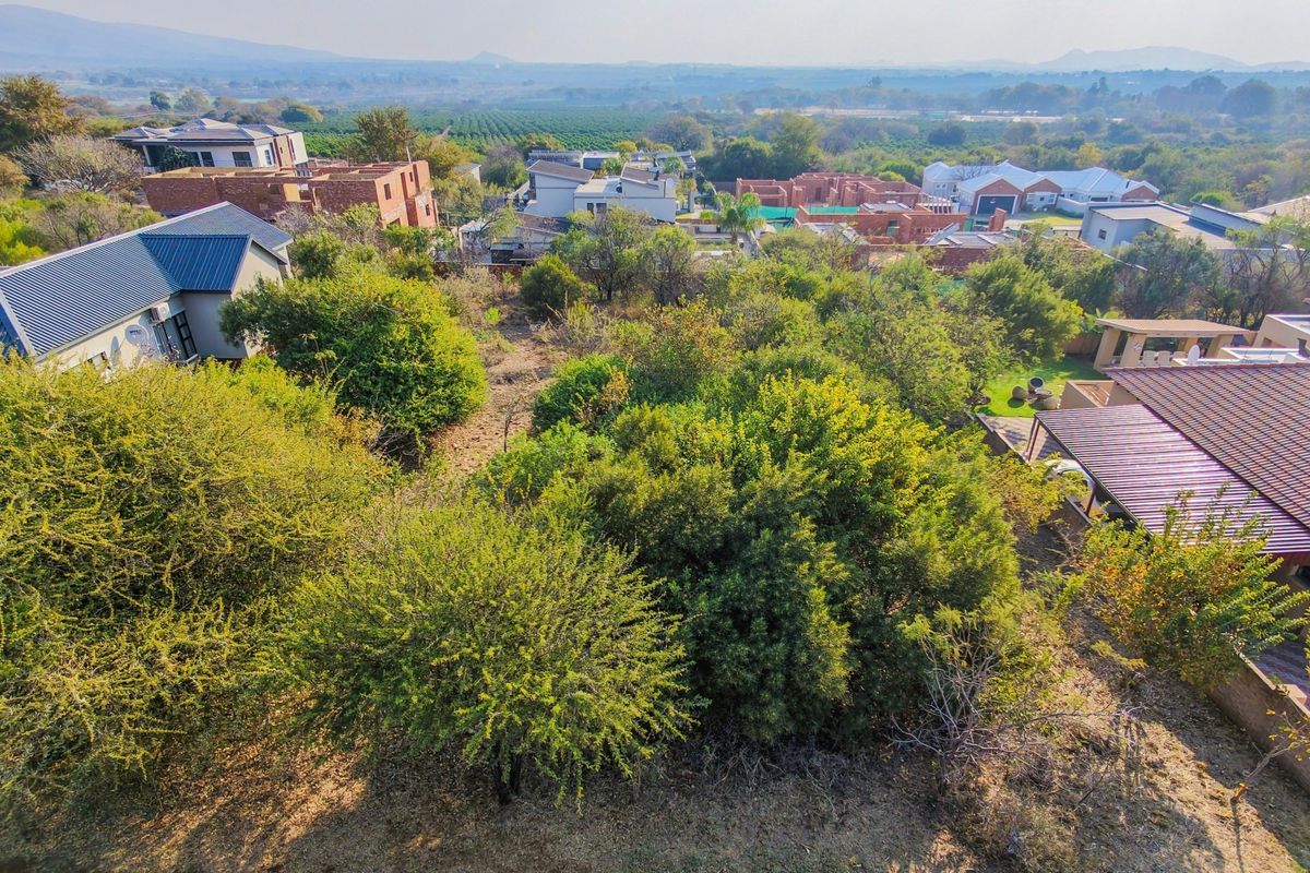 An aerial view of a vacant residential plot surrounded by established trees and neighboring residential properties in a secure estate.