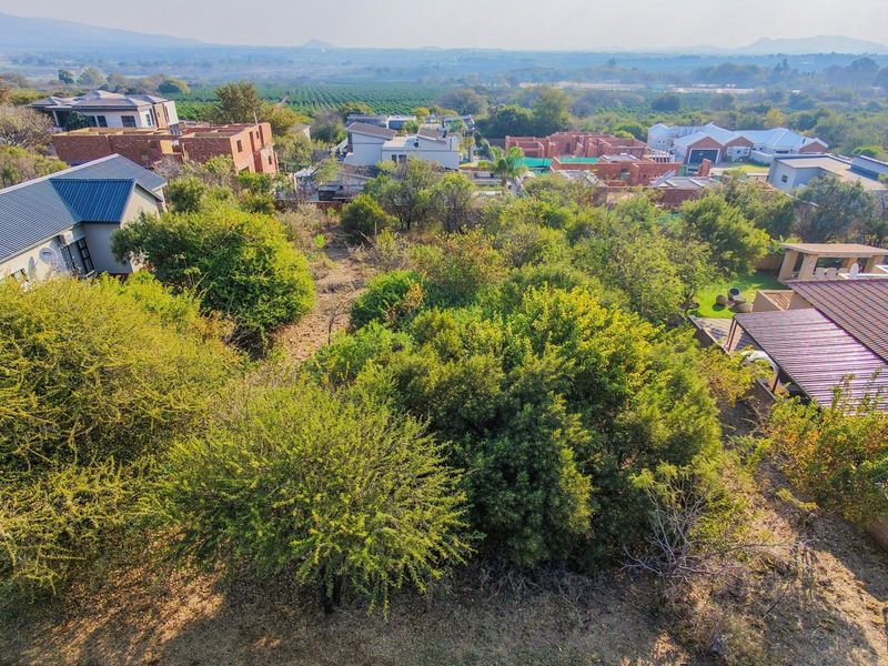 An aerial view of a vacant residential plot surrounded by established trees and neighboring residential properties in a secure estate.