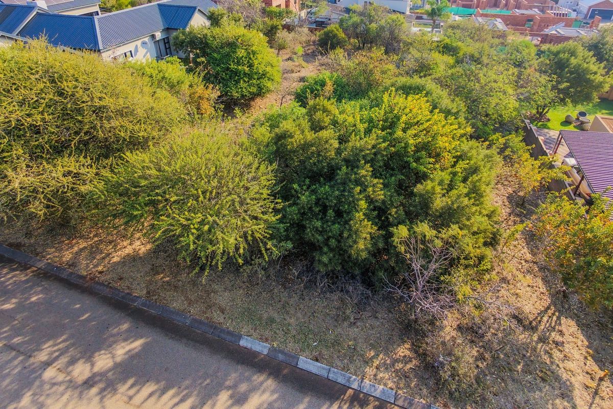 Aerial view of a vacant residential plot featuring established indigenous trees and vegetation, situated adjacent to a paved road with kerbing.