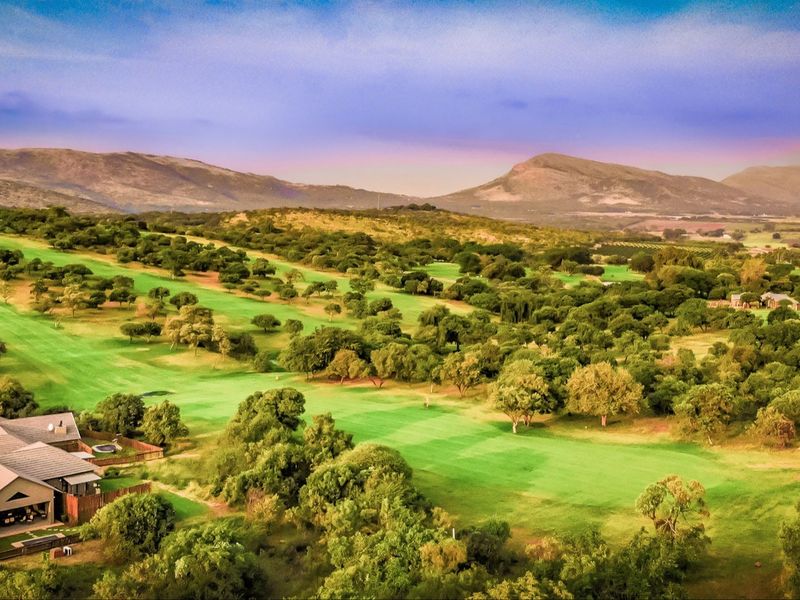 Aerial view of a residential property situated on a scenic golf course with expansive green fairways and mountain views in the background.