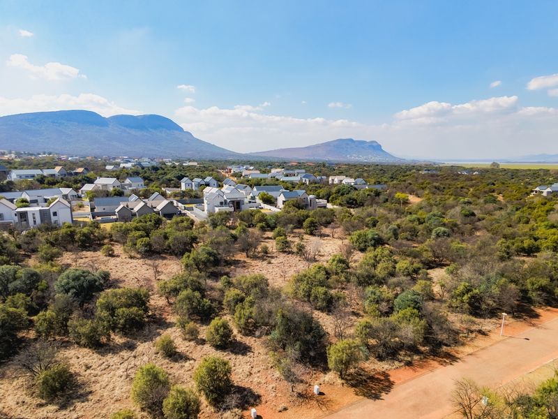Aerial view of a residential estate featuring natural bushveld vegetation, surrounding homes, and mountain vistas in the distance.