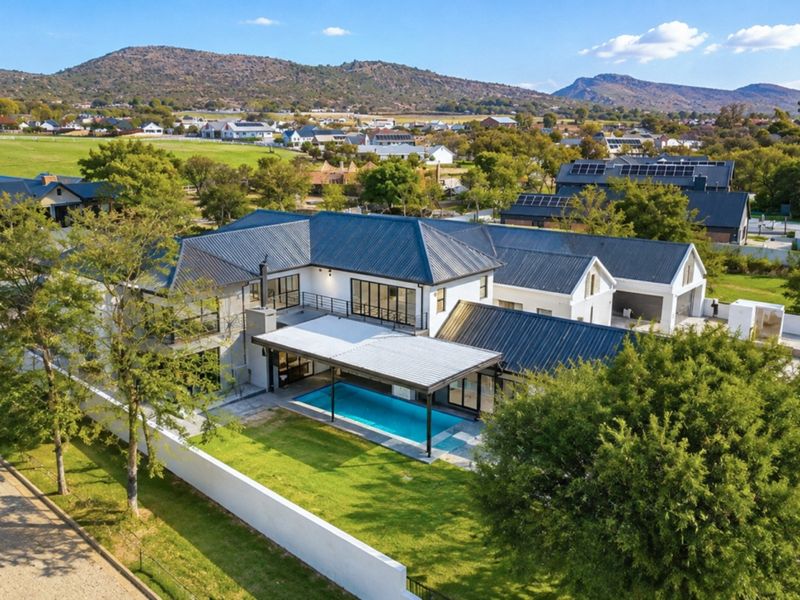 Aerial view of a modern residential property featuring a swimming pool, covered patio, metal roofing, and solar panels within a landscaped estate setting.
