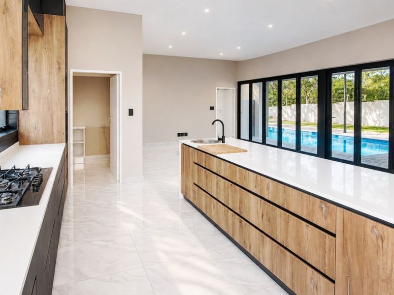 Modern, spacious kitchen featuring a large island, stone countertops, gas hob, and sleek cabinetry, with direct access to the pool area through sliding doors.