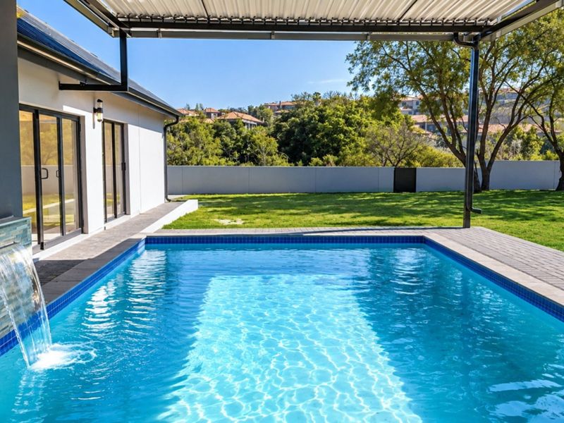 A well-maintained swimming pool with a water feature, set against a landscaped garden and a covered patio area.