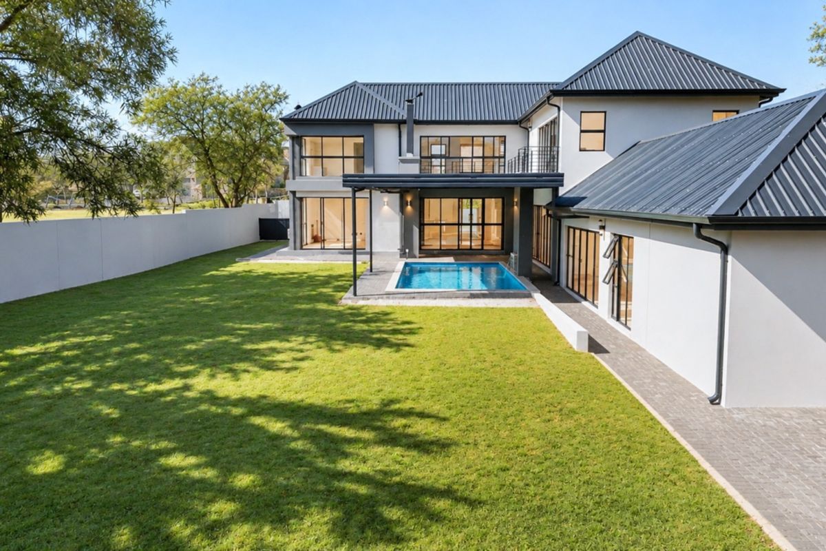 A modern double-story residence featuring a spacious rear garden, a swimming pool, and a paved patio area with large glass sliding doors.