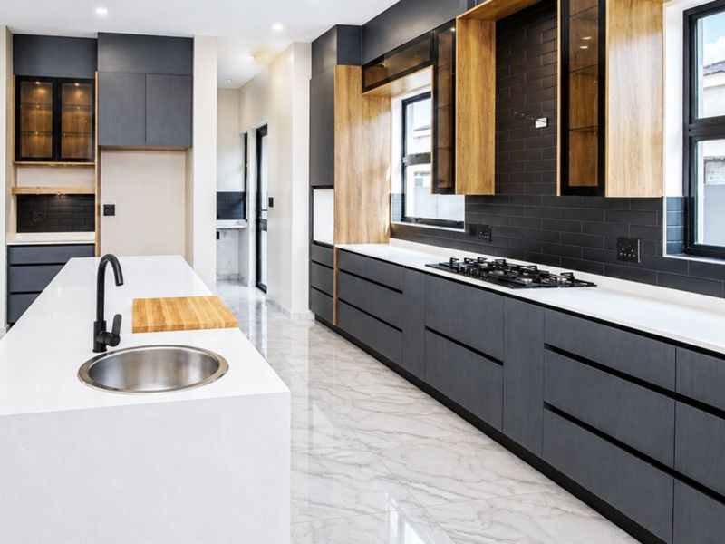 Modern kitchen featuring dark cabinetry, light stone countertops, a central island with a sink, gas hob, and sleek tiled backsplash.