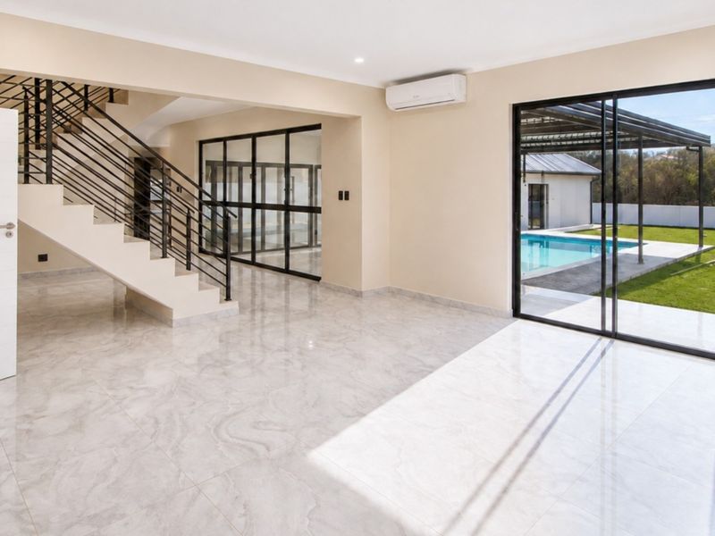 Spacious open-plan living area featuring modern tiled floors, a sleek staircase with metal balustrades, and large sliding doors opening to the pool and garden.