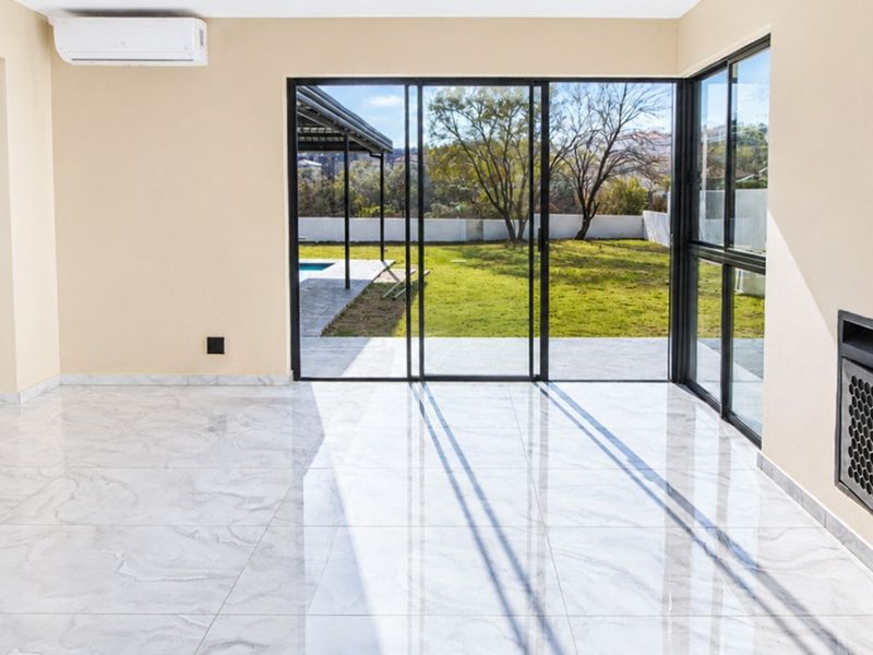 Bright and spacious living area featuring polished marble-look floor tiles, a built-in fireplace, and large sliding glass doors opening to the garden.