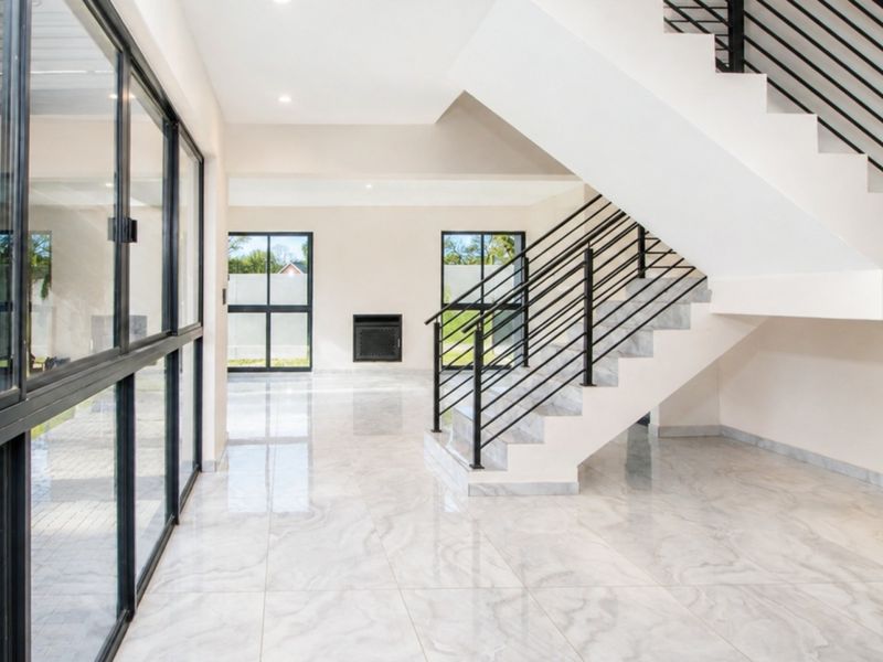 Spacious, modern open-plan living area featuring polished marble-look tiles, a striking black staircase, and large windows providing abundant natural light.