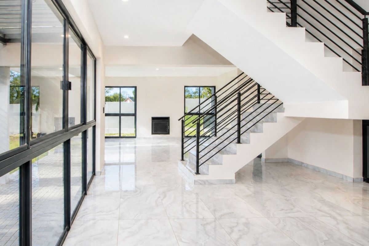 Spacious, modern open-plan living area featuring polished marble-look tiles, a striking black staircase, and large windows providing abundant natural light.