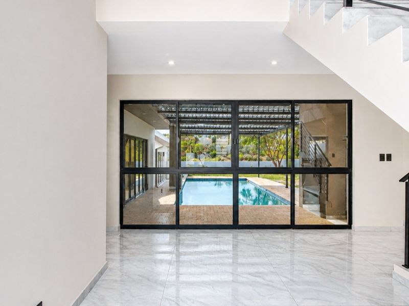 Spacious modern entrance hall featuring polished marble flooring, a sleek staircase, and large glass doors providing a clear view of the outdoor pool area.