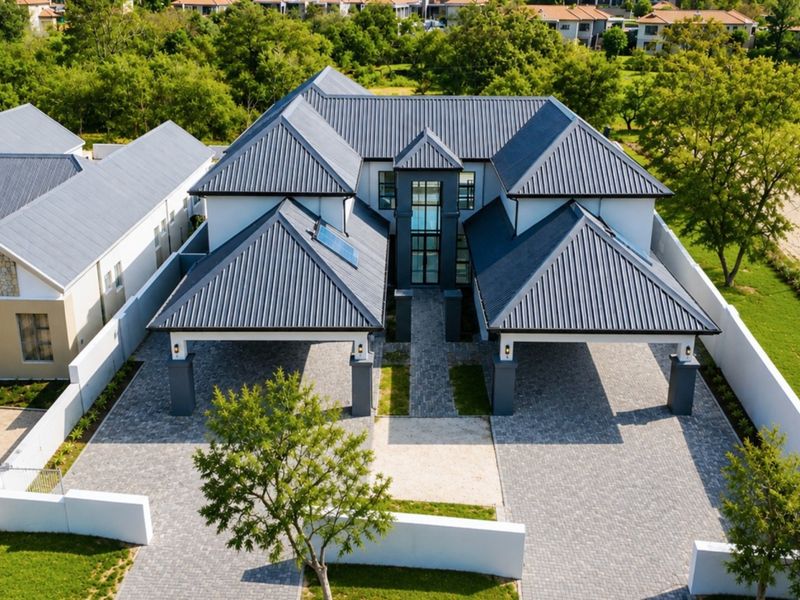 Aerial view of a modern residential property featuring a large metal roof, extensive paved driveway, and covered parking areas within a landscaped estate.