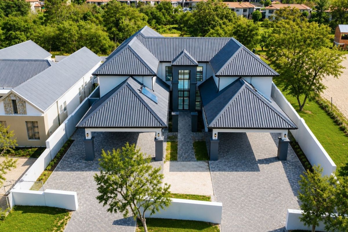 Aerial view of a modern residential property featuring a large metal roof, extensive paved driveway, and covered parking areas within a landscaped estate.
