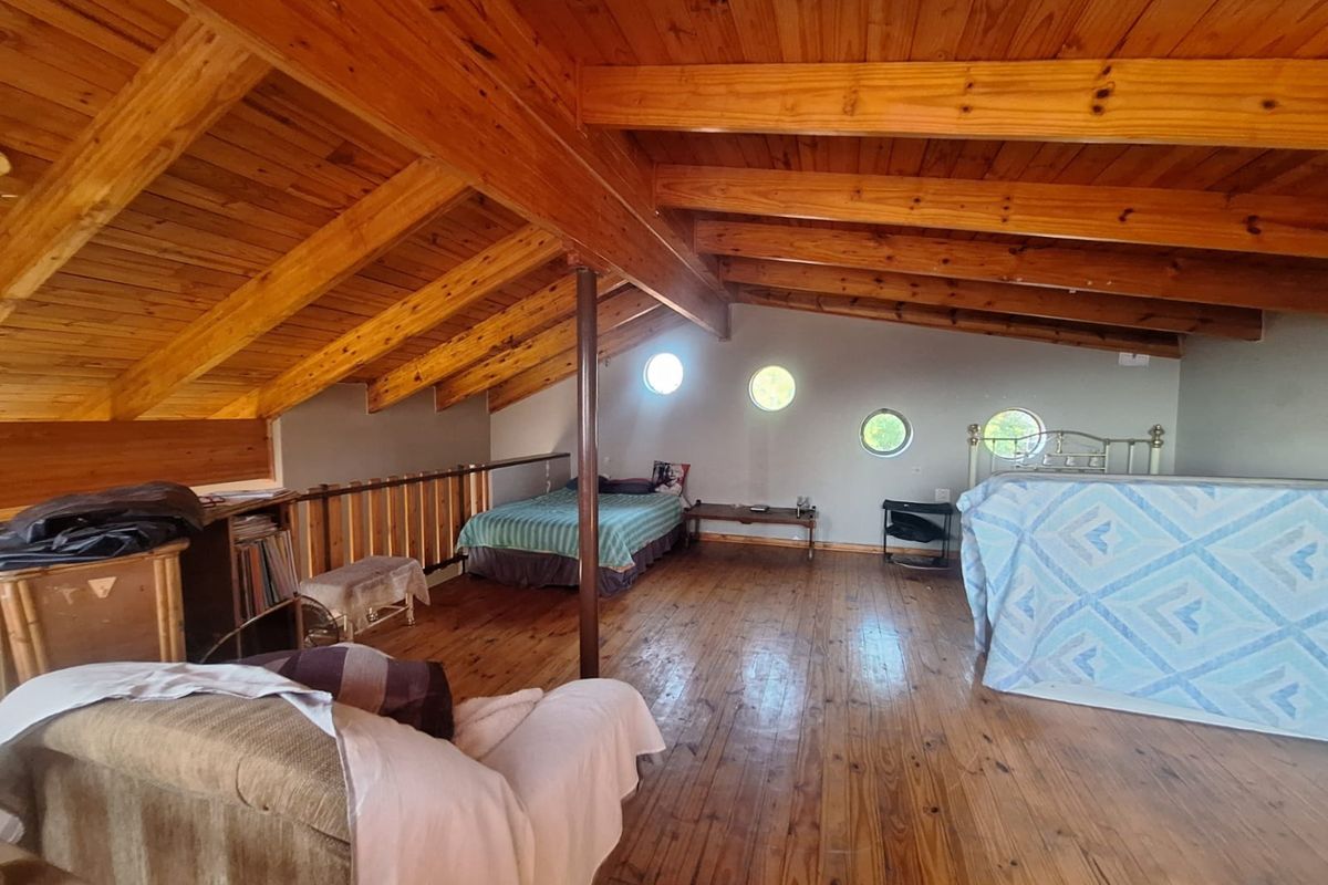 Spacious loft-style bedroom featuring exposed timber vaulted ceilings, warm wood flooring, and unique circular porthole windows.