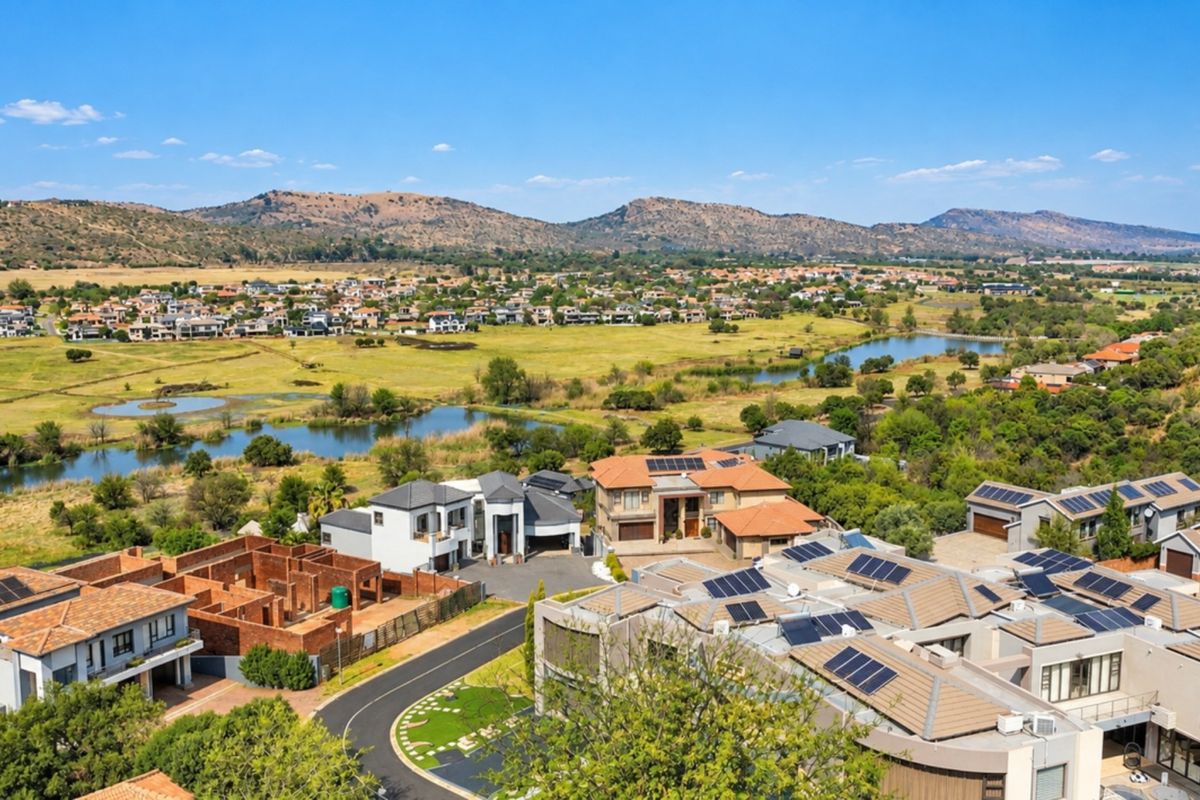 An aerial view of a residential estate featuring multiple homes with solar panel installations, surrounded by landscaped grounds and natural water features.