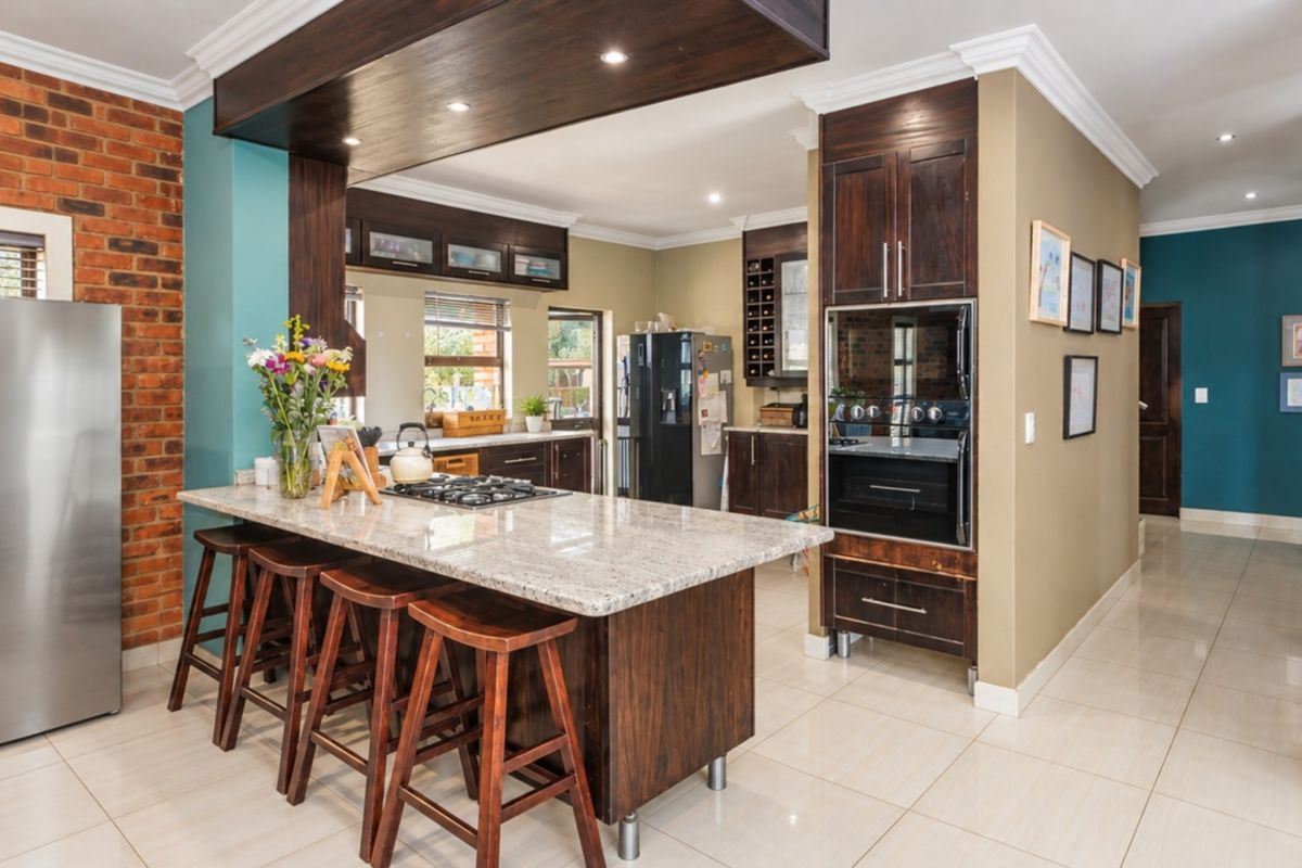 Modern kitchen featuring dark wood cabinetry, granite countertops, a central island with a gas hob, and a built-in oven, complemented by exposed brick accents.