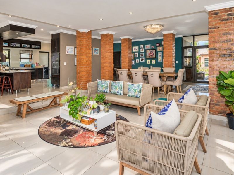 Spacious open-plan living, dining, and kitchen area featuring exposed brick columns, modern tiled flooring, and seamless access to outdoor spaces through sliding glass doors.