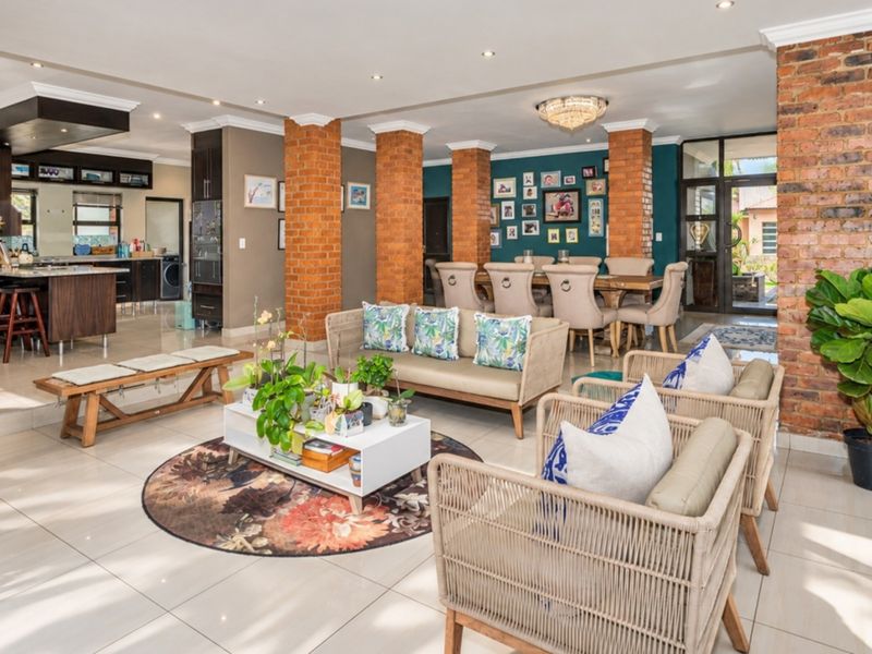 Spacious open-plan living and dining area featuring exposed brick columns, modern tiled flooring, and a well-appointed kitchen with a central island.