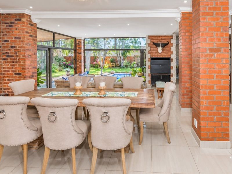 Spacious dining area featuring exposed brick columns, tiled flooring, and large glass sliding doors that provide a seamless transition to the outdoor pool area.