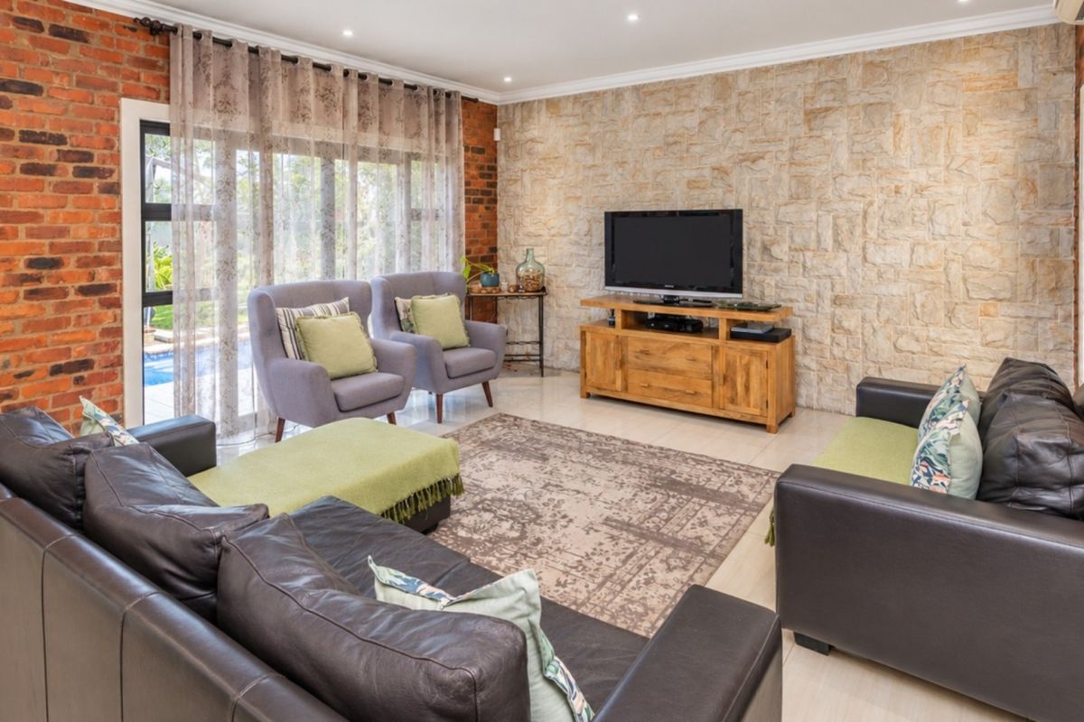A well-maintained living room featuring a striking stone cladding feature wall, exposed brick accents, tiled flooring, and large sliding doors leading to the outdoors.