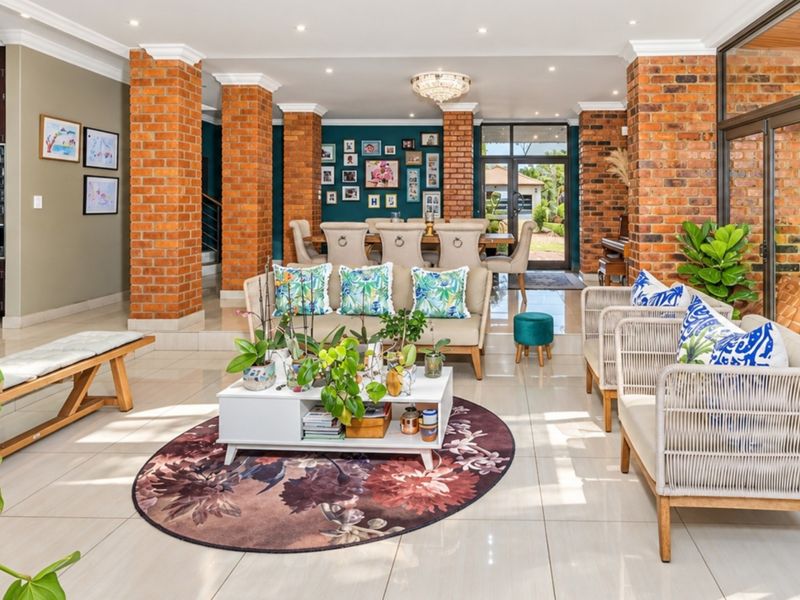 Spacious open-plan living and dining area featuring exposed brick columns, polished tile flooring, and large aluminium stacker doors leading to the outdoors.