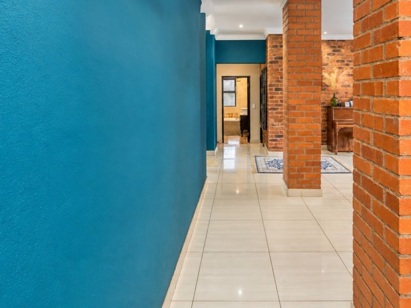 A spacious hallway featuring polished tile flooring, striking blue accent walls, and exposed brick columns leading towards a bathroom.