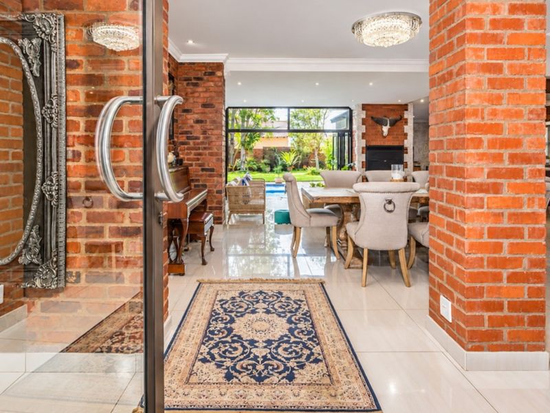 Spacious open-plan living and dining area featuring striking exposed brick columns, polished porcelain flooring, and large glass doors opening to the garden and pool.