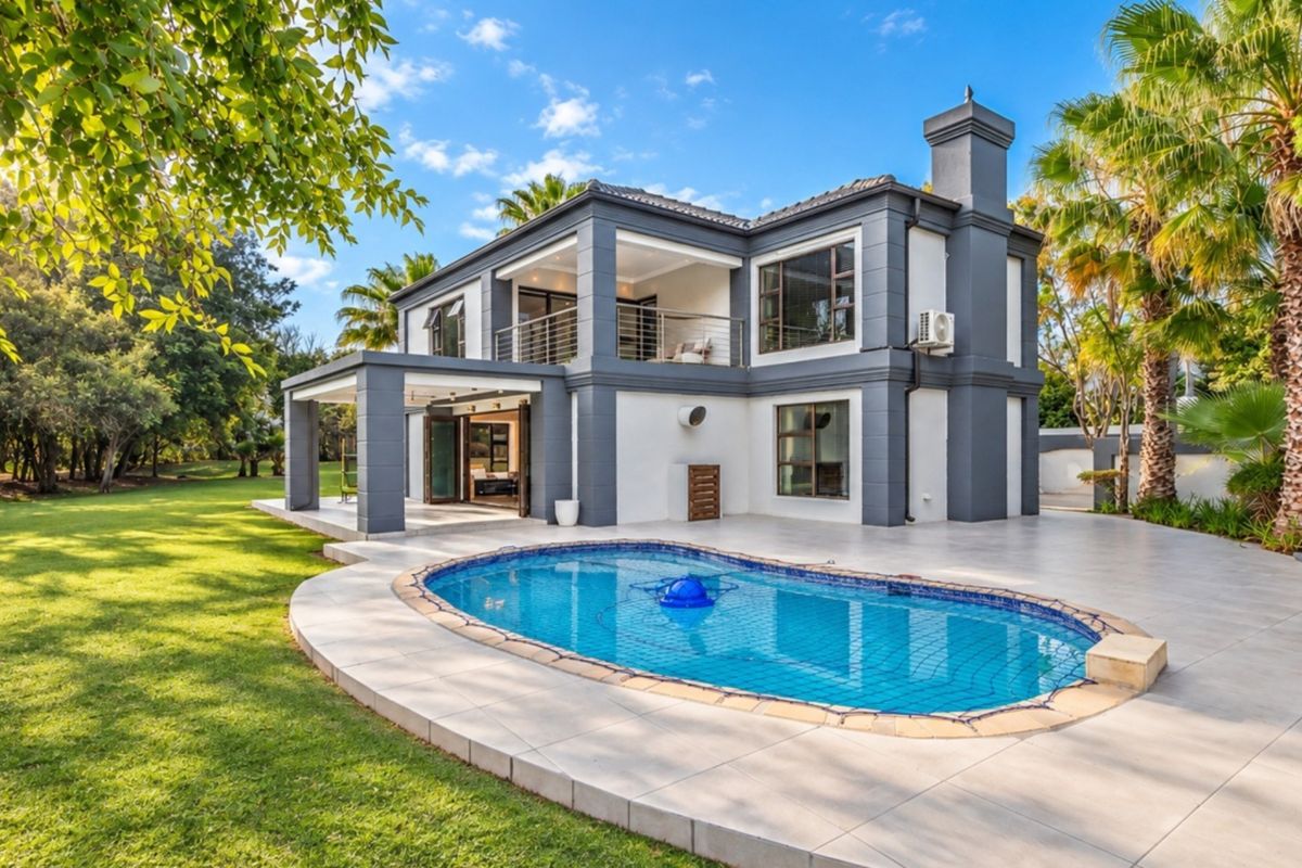 Rear view of a modern two-story house featuring a swimming pool, tiled patio area, upper-level balcony, and a well-maintained garden.