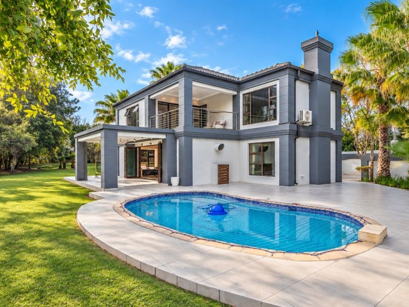 Rear view of a modern two-story house featuring a swimming pool, tiled patio area, upper-level balcony, and a well-maintained garden.