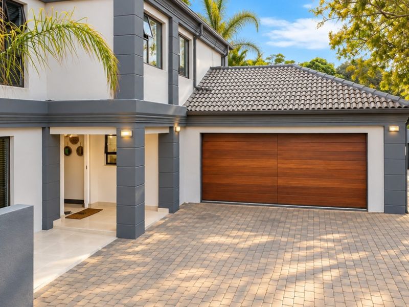 Modern double-storey home exterior featuring a paved driveway, timber-look garage door, and a welcoming covered entrance.