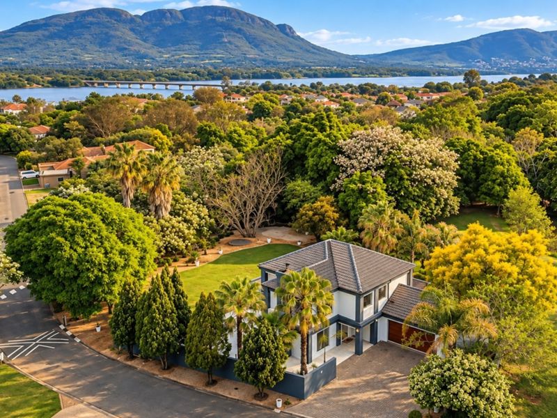Aerial view of a well-maintained residential property featuring a tiled roof, paved driveway, double garage, and expansive landscaped garden in a scenic estate setting.