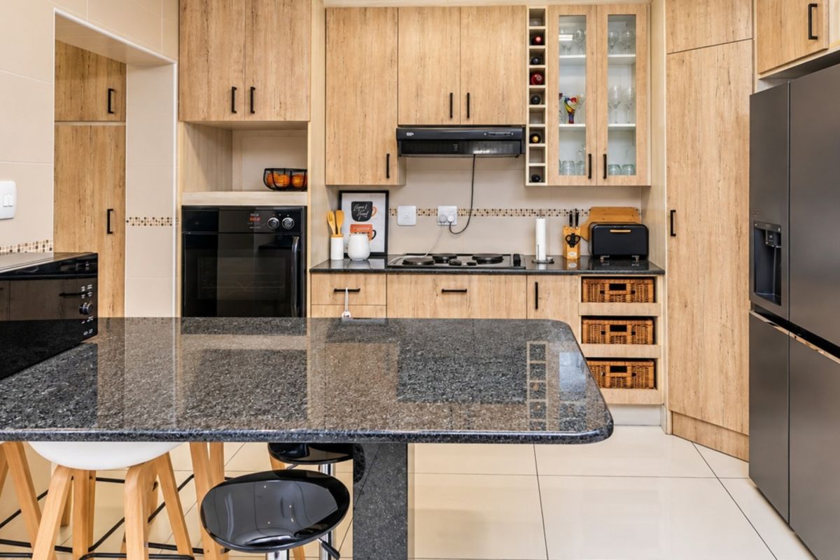 Modern kitchen featuring light wood cabinetry, granite countertops, built-in oven, hob, extractor fan, and tiled flooring.