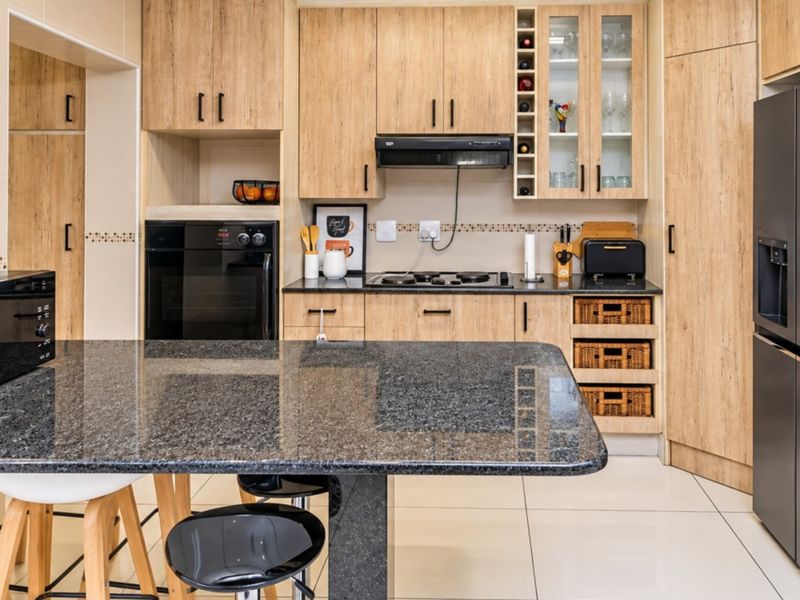 Modern kitchen featuring light wood cabinetry, granite countertops, built-in oven, hob, extractor fan, and tiled flooring.