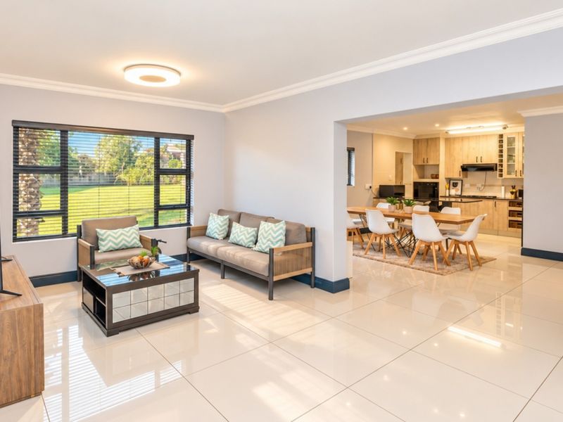 Spacious open-plan living and dining area featuring polished floor tiles, modern kitchen cabinetry, and large windows overlooking the garden.