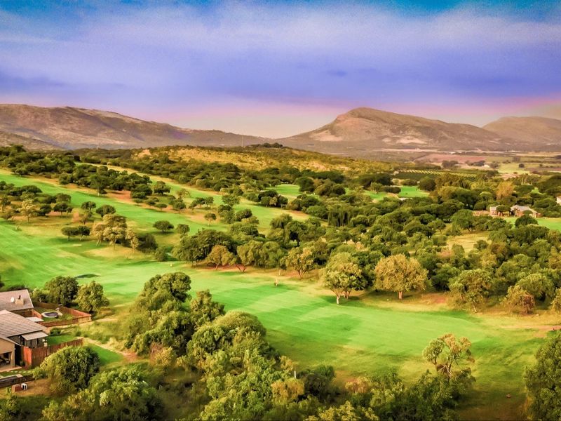 An elevated aerial view showcasing the expansive golf course landscape, lush greenery, and scenic mountain backdrop surrounding the residential property.