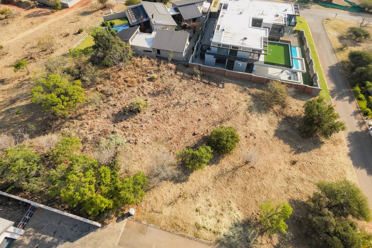 An aerial view of a vacant residential plot featuring native vegetation, situated in a developed estate with neighboring modern homes.